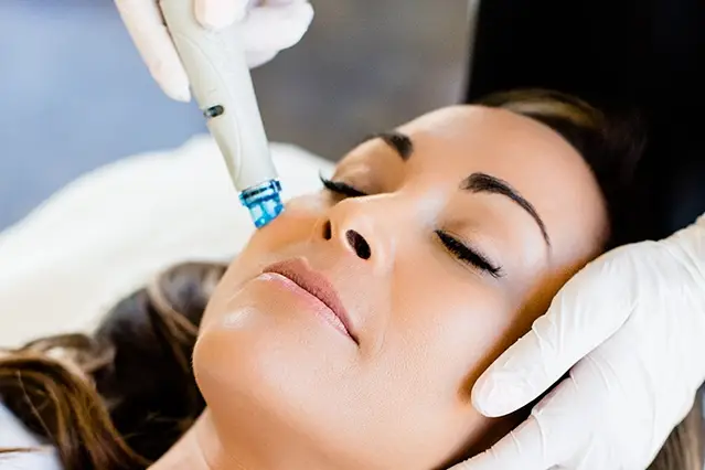 Woman receiving a facial treatment with a handheld device.