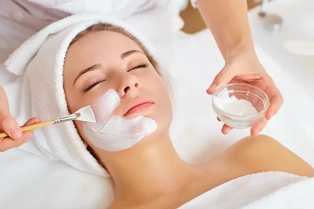Woman receiving a facial treatment with a brush and cream.