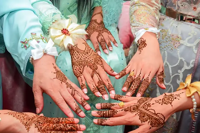 Decorative henna designs on five hands wearing elegant clothing.