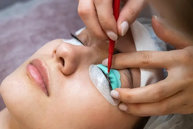 Eyelash extension application on woman with protective pads under her eyes.