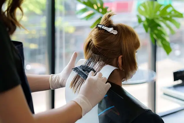 Hair stylist applying color to a client's hair in a salon.